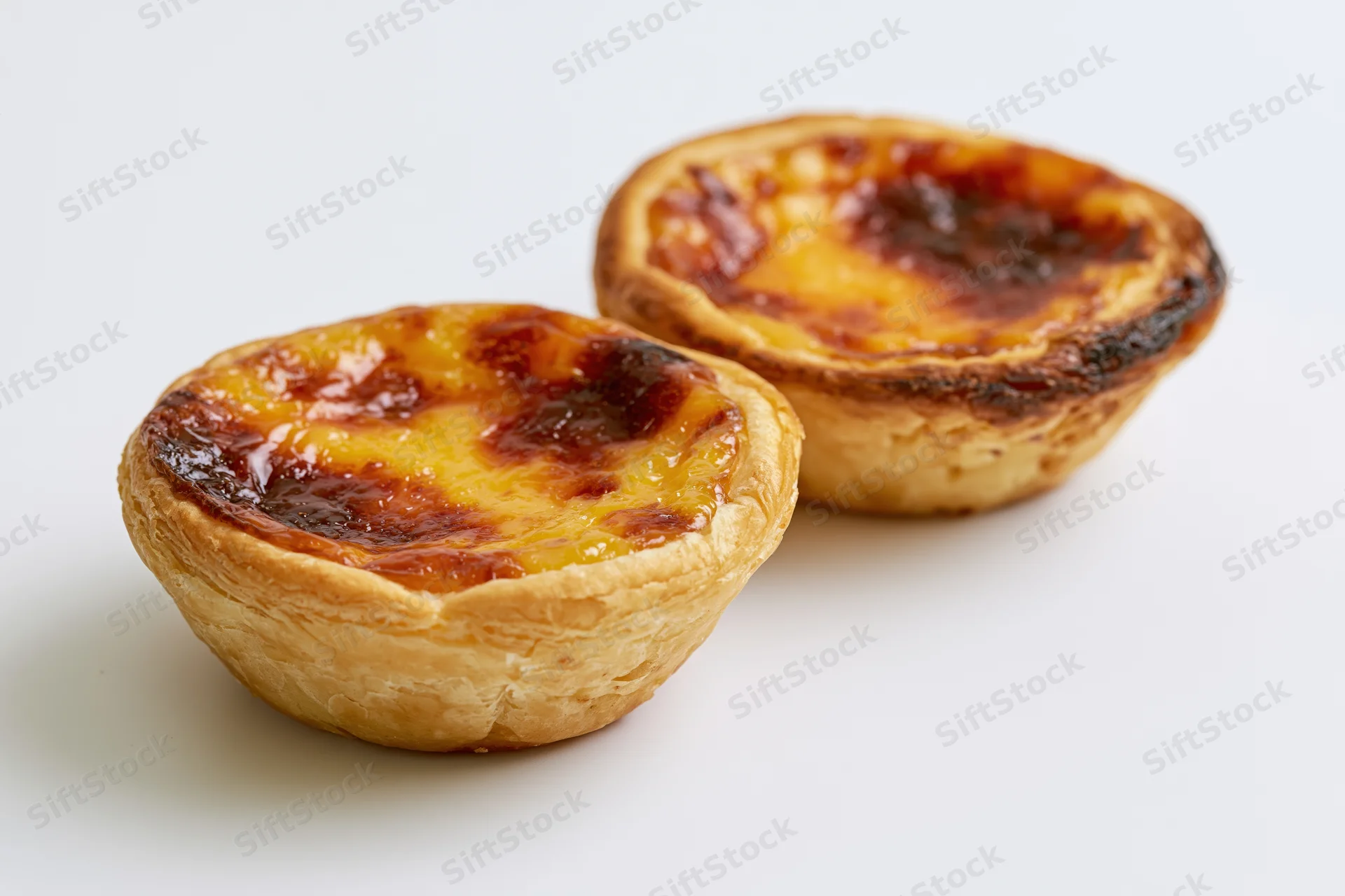 Two portuguese pastel de nata egg tarts placed close together on white surface