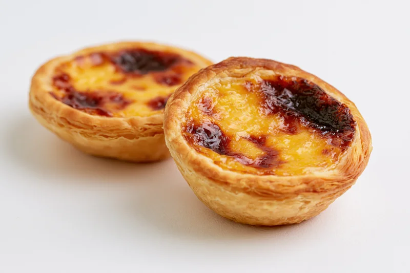 Two portuguese pastel de nata egg tarts placed close together on white surface