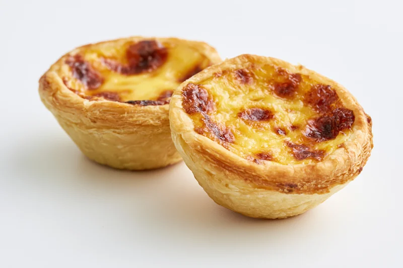 Two portuguese pastel de nata egg tarts placed close together on white surface