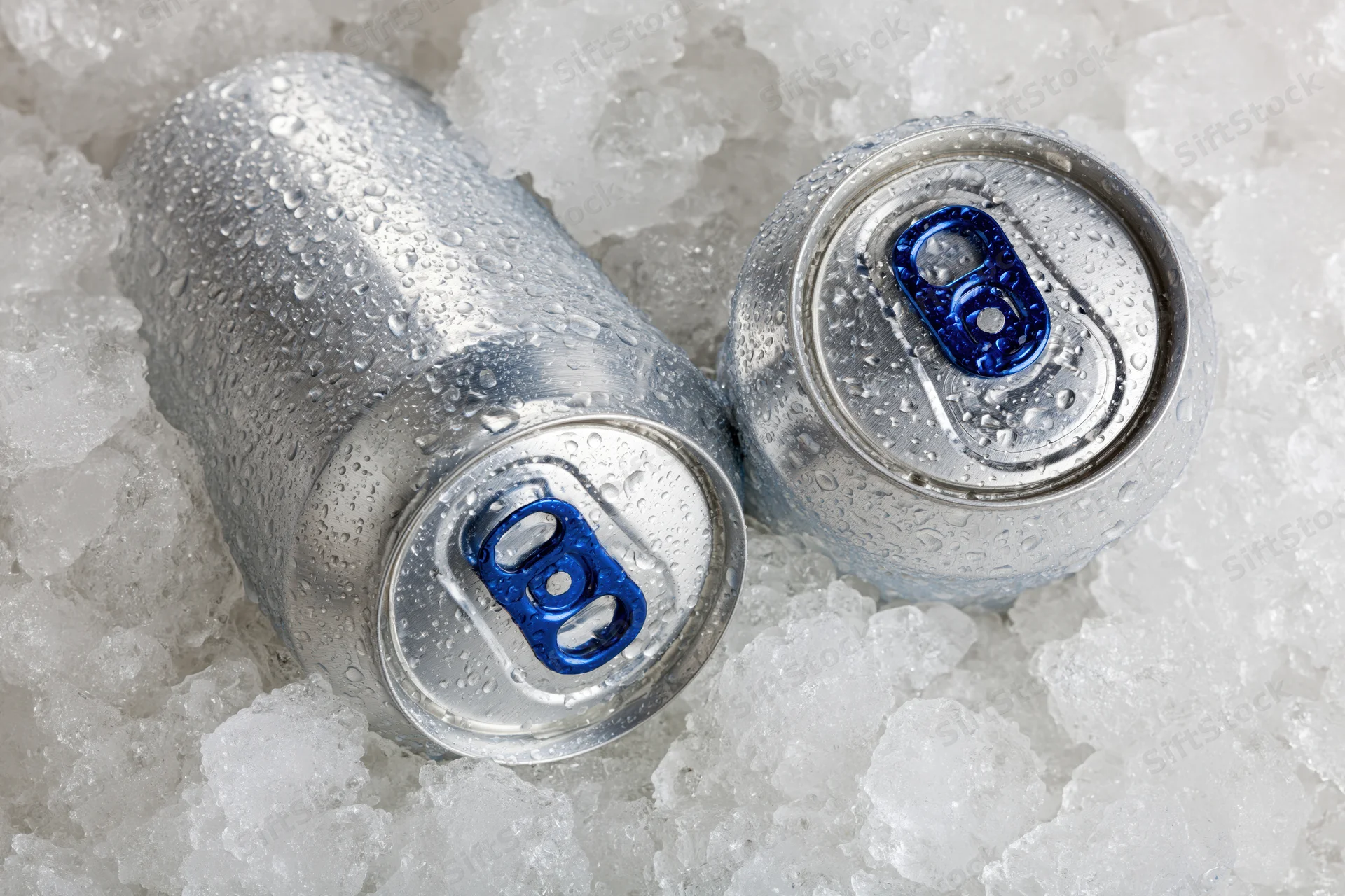 Two aluminum beverage cans with blue pull tabs resting in crushed ice
