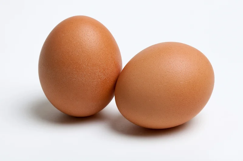 Two brown chicken eggs resting side by side on a plain white surface