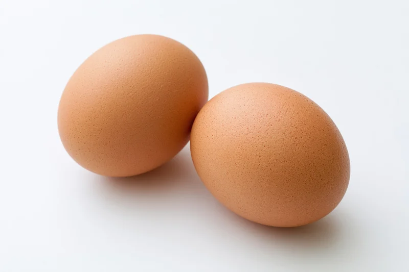 Two brown chicken eggs resting side by side on a pure white surface
