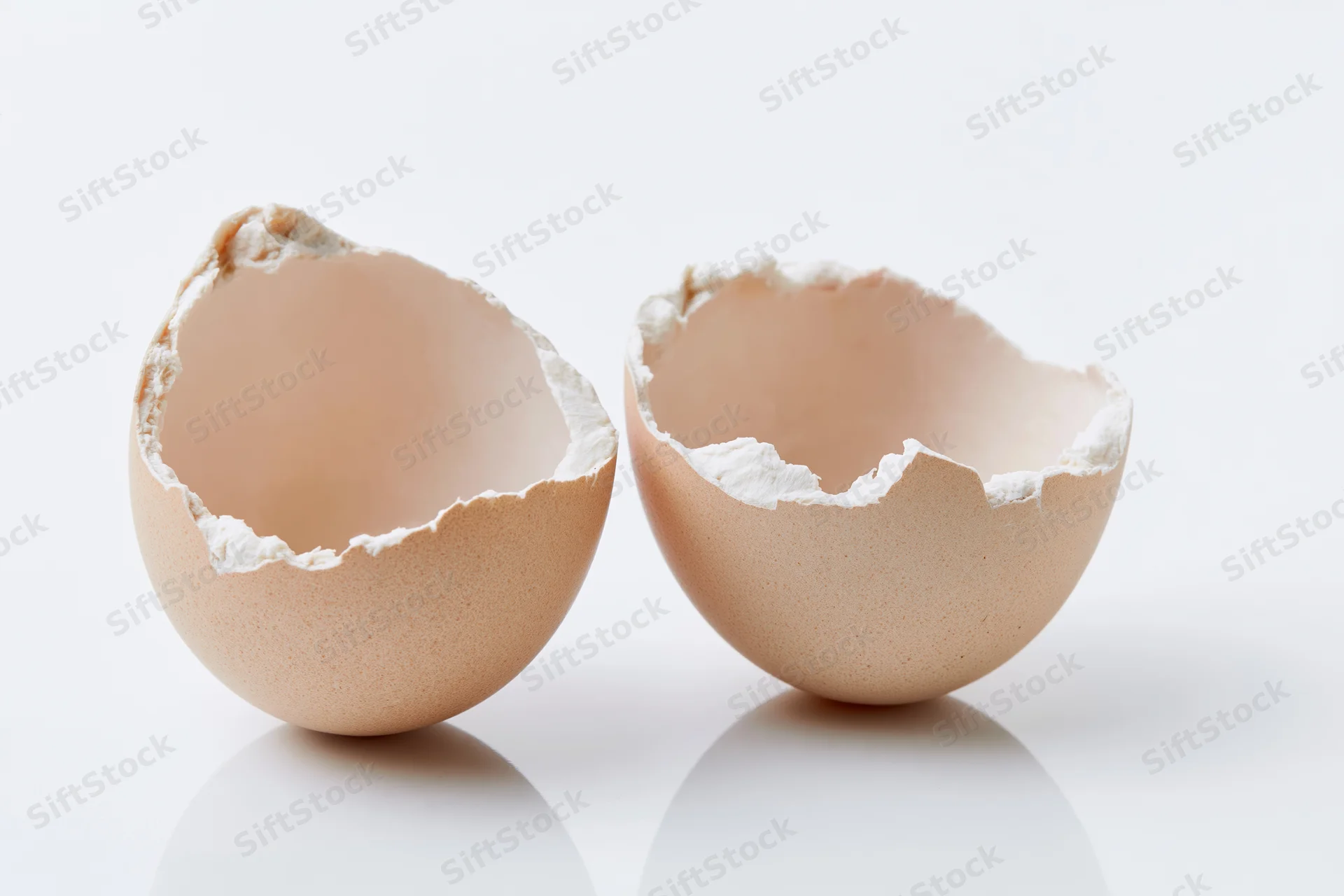 Two cracked eggshell halves split apart and empty placed side by side on white surface
