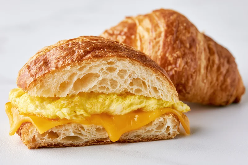 Croissant breakfast sandwich with egg and cheese on white surface