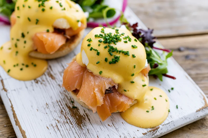 Two eggs benedict with smoked salmon on toasted english muffins served with salad on a rustic white board