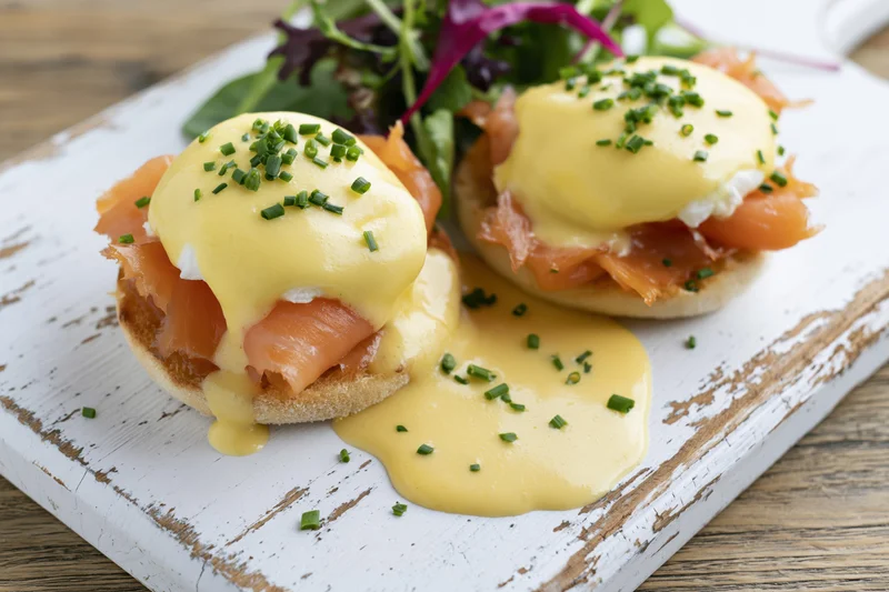 Two eggs benedict with smoked salmon on toasted english muffins served with salad on a white distressed wooden board