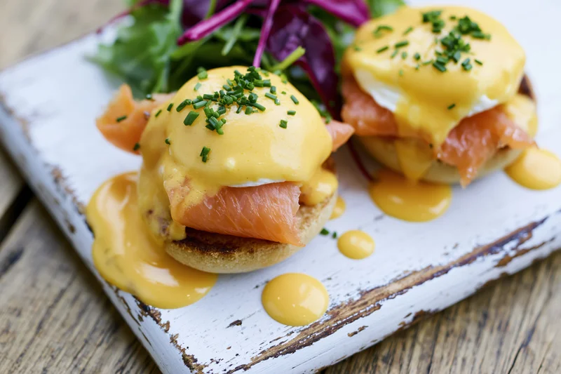 Two eggs benedict with smoked salmon on toasted english muffins served with mixed greens on a rustic white plate