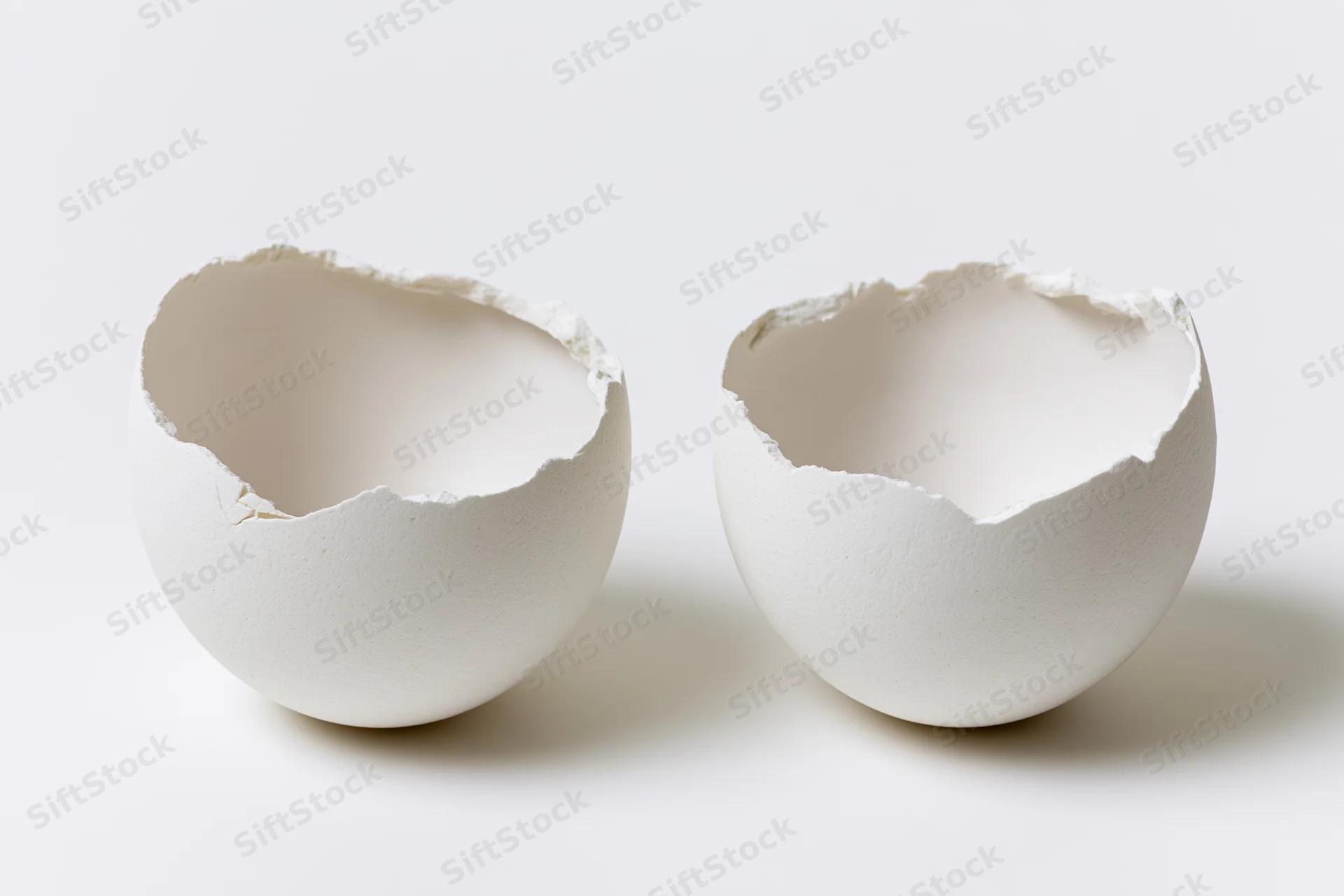 Two empty white eggshell halves split open and placed side by side on a plain white surface
