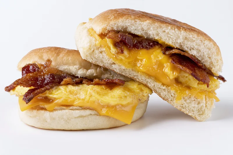 Two halves of a breakfast sandwich on a soft kaiser roll stacked on white background