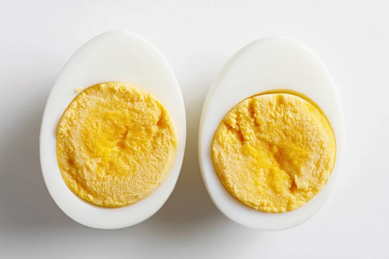 Two halves of a hard-boiled egg cut face up on a white surface
