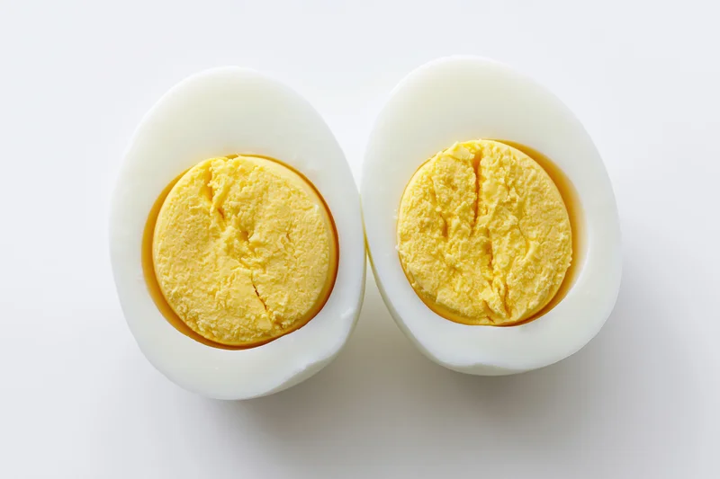 Two halves of a hard-boiled egg cut face up on a white surface