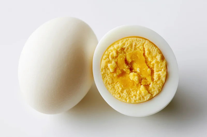 Two hard-boiled eggs on white surface, one whole and one halved to show yolk and white interior