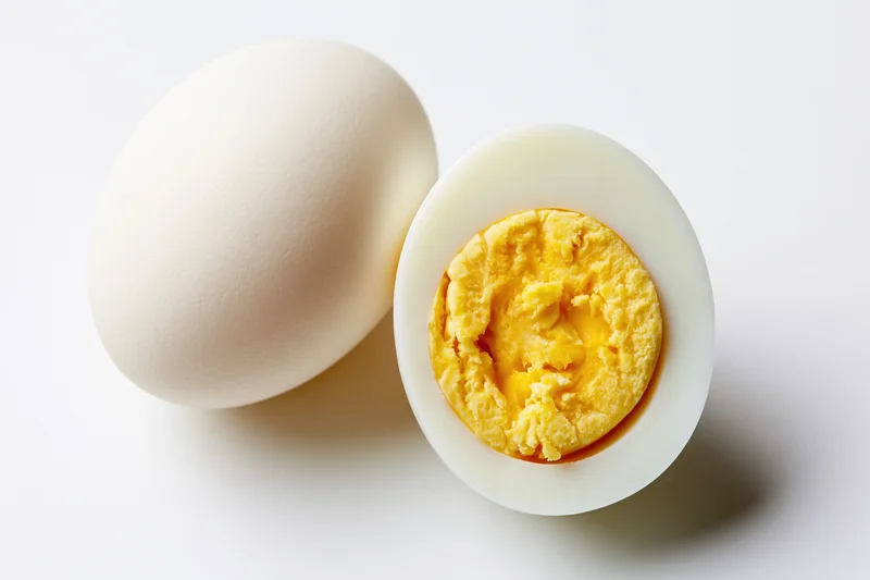 Two hard-boiled eggs, one whole and one halved, on a plain white surface