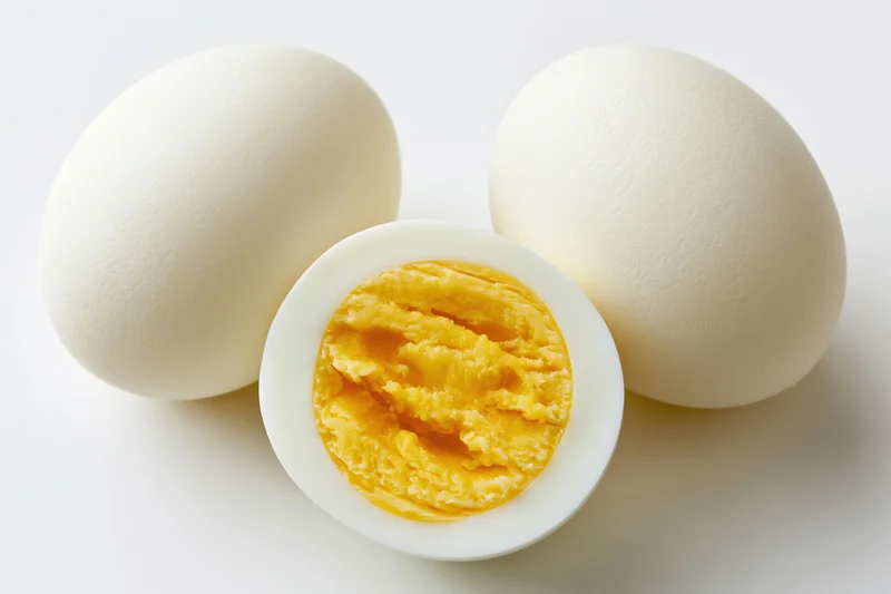 Two hard-boiled eggs on white background one halved showing yolk and white