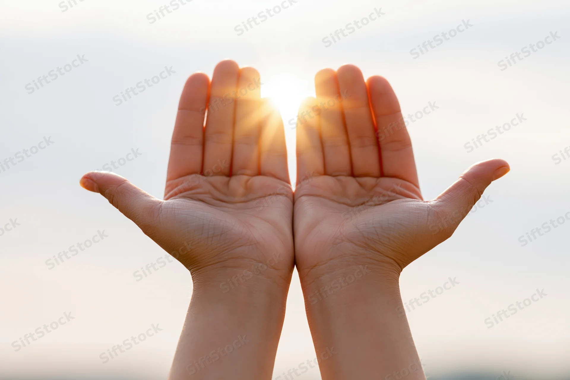 Open hands raised upward toward bright glowing sun in sky