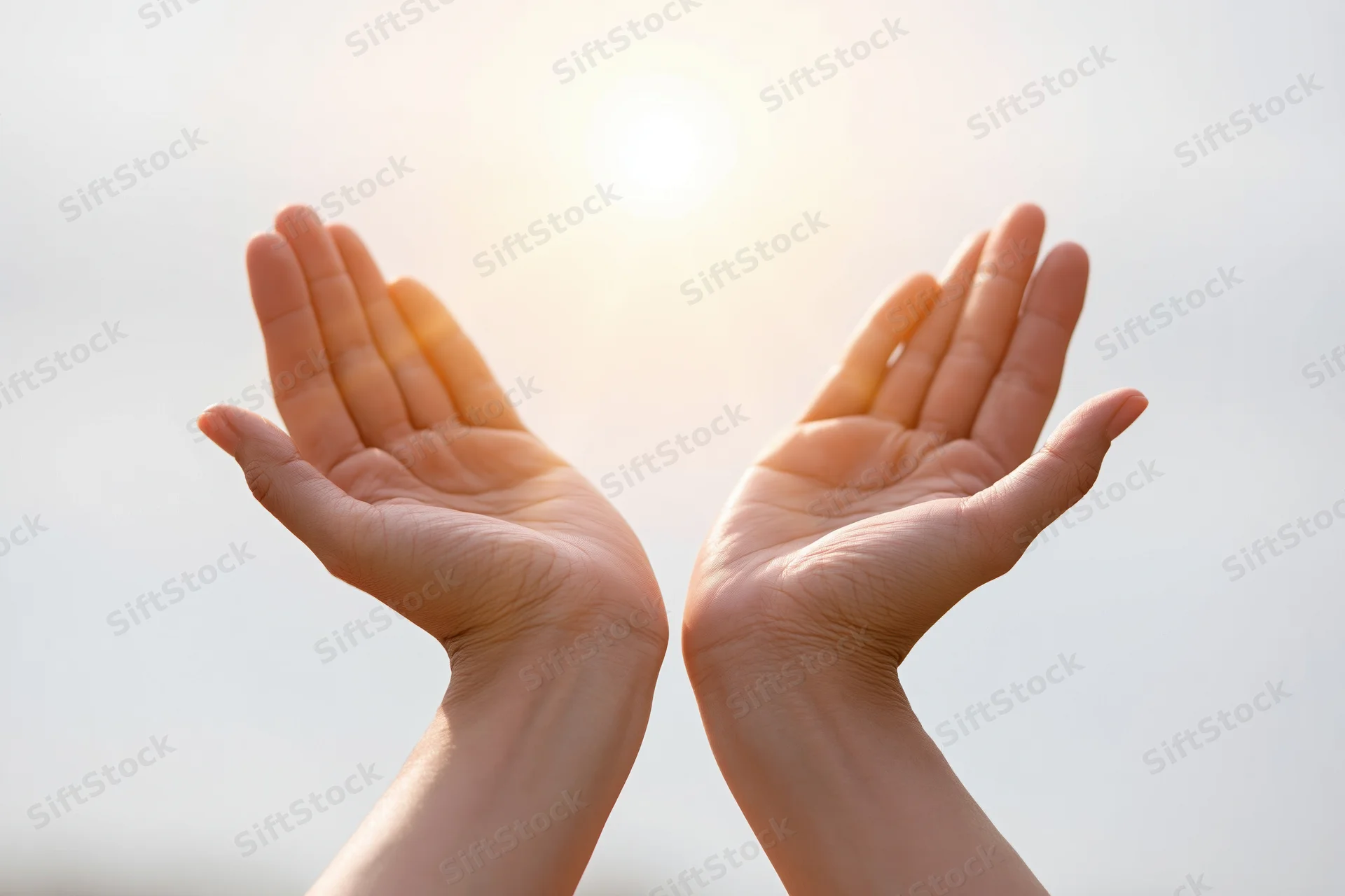 Open cupped hands raised upward toward a bright glowing sun in the sky