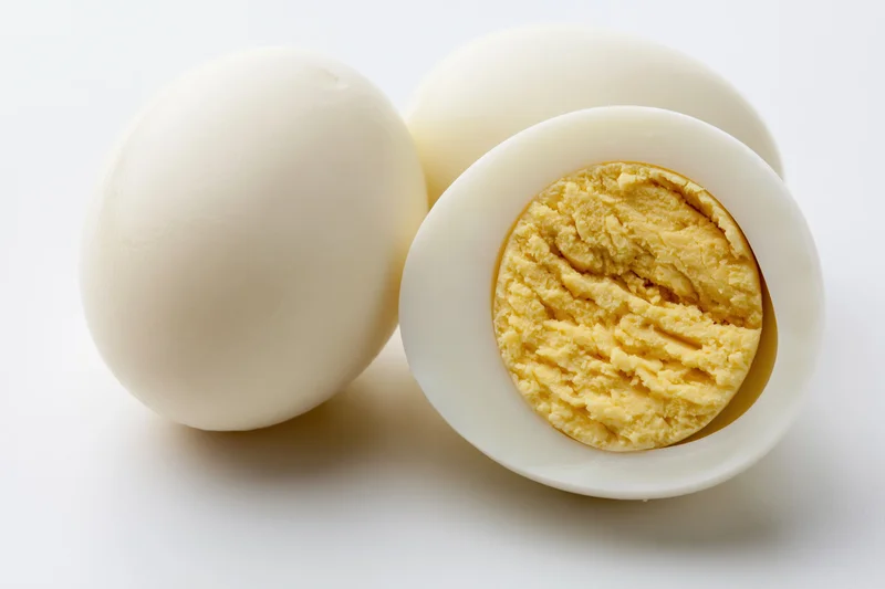 Two peeled hard-boiled eggs beside a halved egg showing the yolk on a white surface