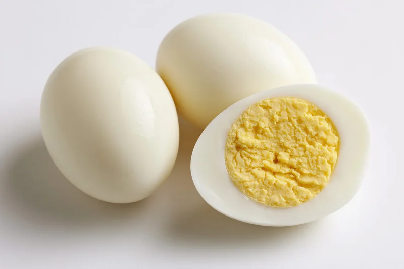 Three peeled hard-boiled eggs with one halved to show the yolk on a white surface