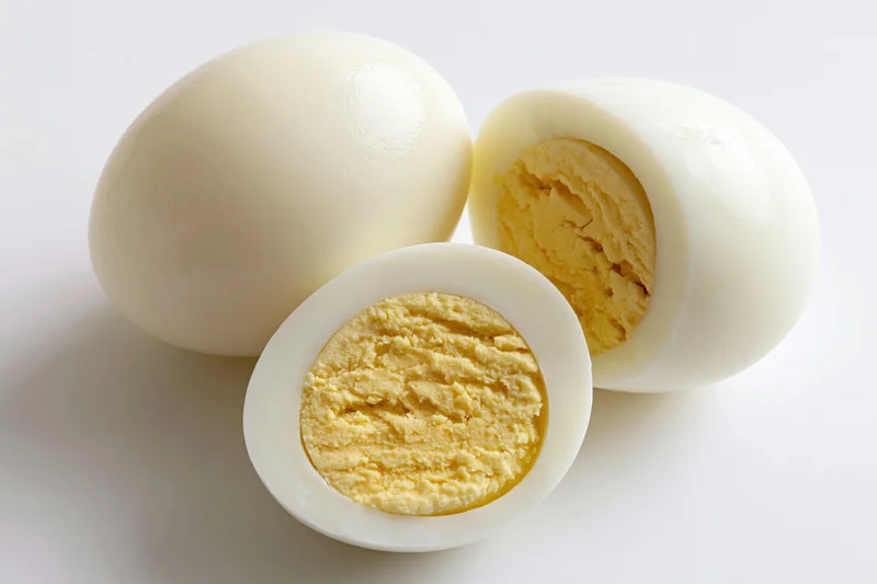 Two peeled hard-boiled eggs beside a halved egg showing the solid yolk on a white surface