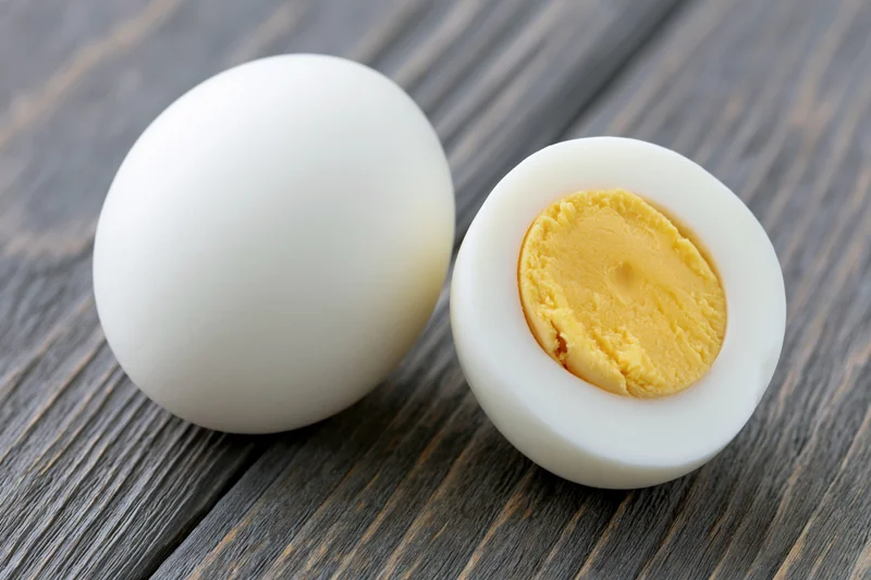 Two peeled hard-boiled eggs one whole and one halved on a gray wooden surface