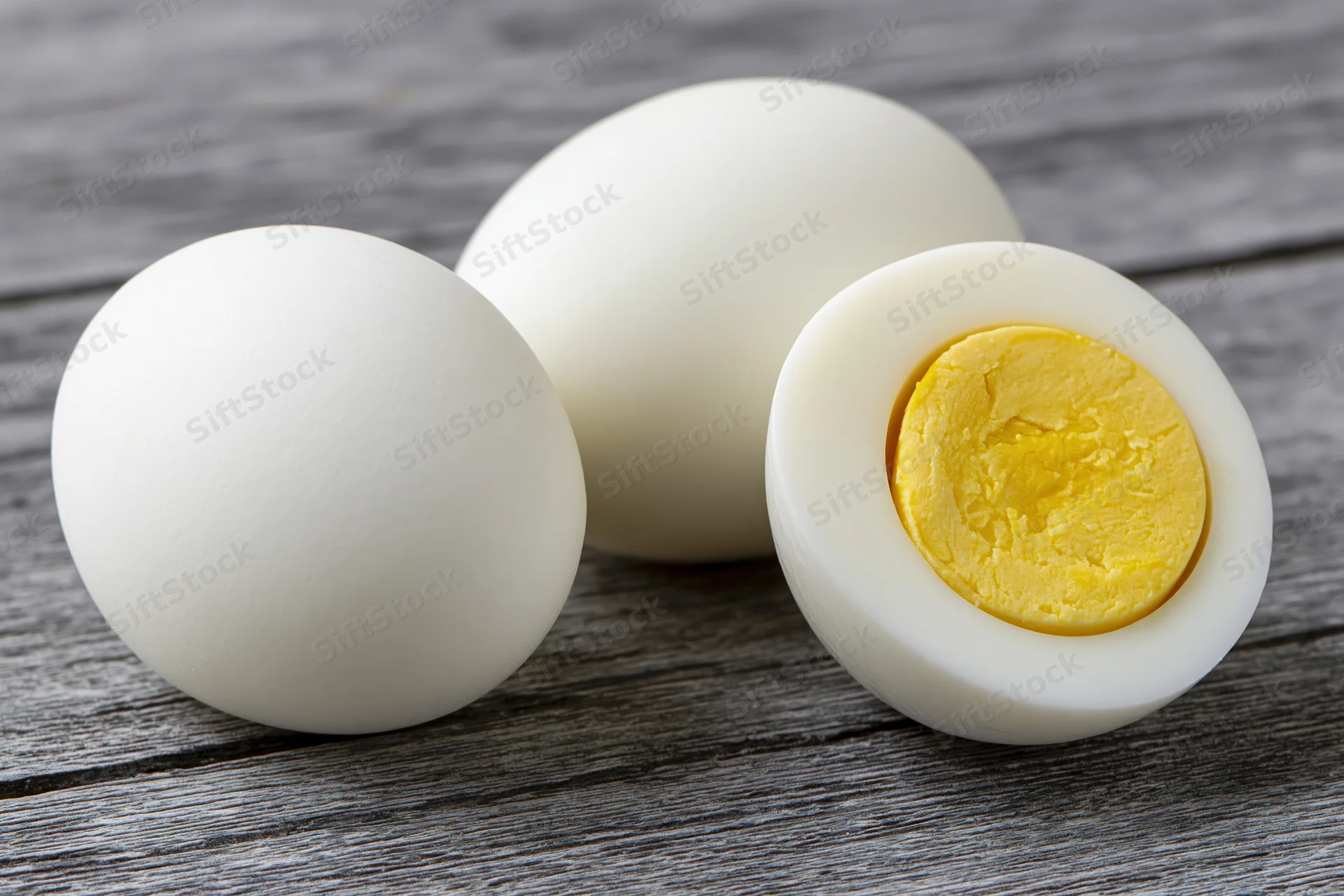 Three peeled hard-boiled eggs, one halved to show yolk, arranged on a gray wooden surface