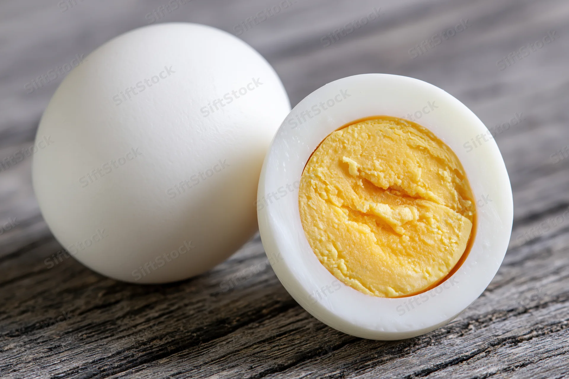 Two peeled hard-boiled eggs one whole and one halved on a grey wooden surface
