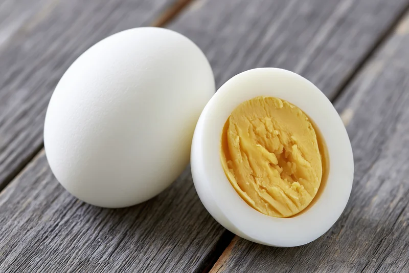 Two peeled hard-boiled eggs one whole and one halved on a gray wooden surface