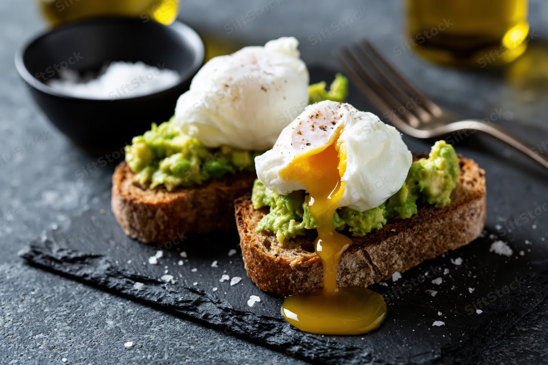Two slices of sourdough toast topped with smashed avocado and poached eggs with runny yolks on a slate plate