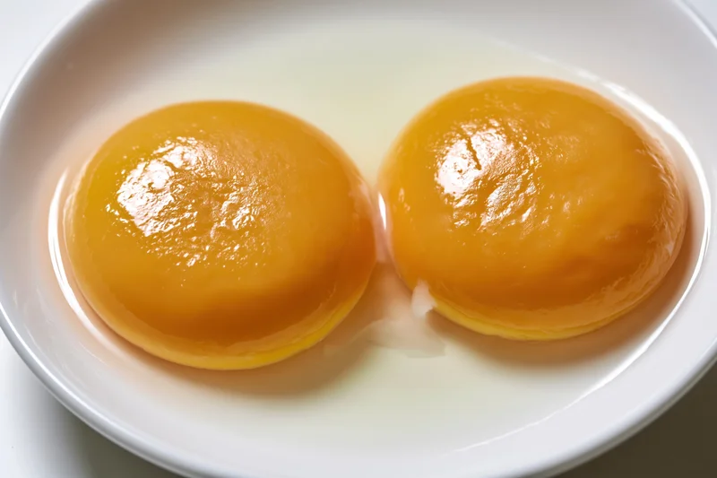 Two raw double egg yolks cracked onto a plain white ceramic plate