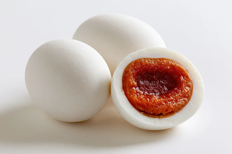Two whole salted duck eggs and one halved to reveal orange yolk on white background