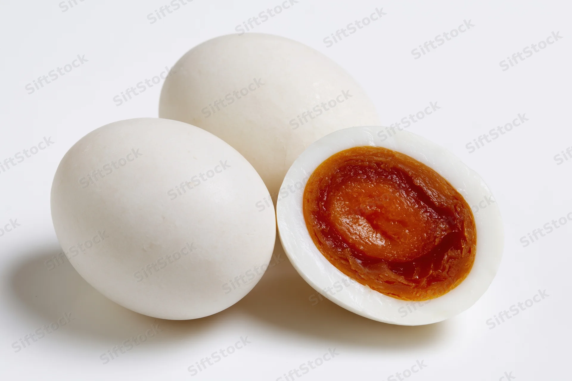 Two whole salted duck eggs and one halved egg showing orange yolk on white background