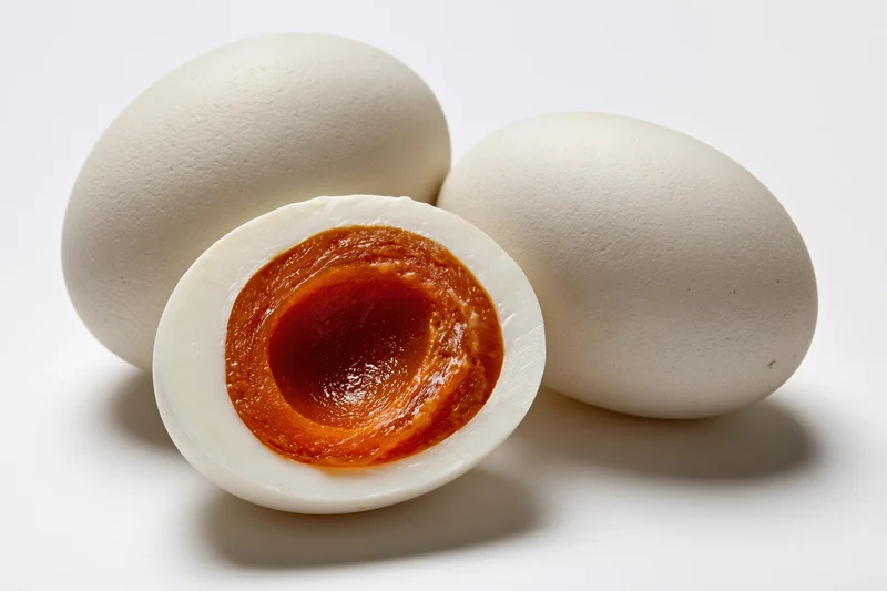 Halved salted duck egg revealing orange yolk beside two whole eggs on white background