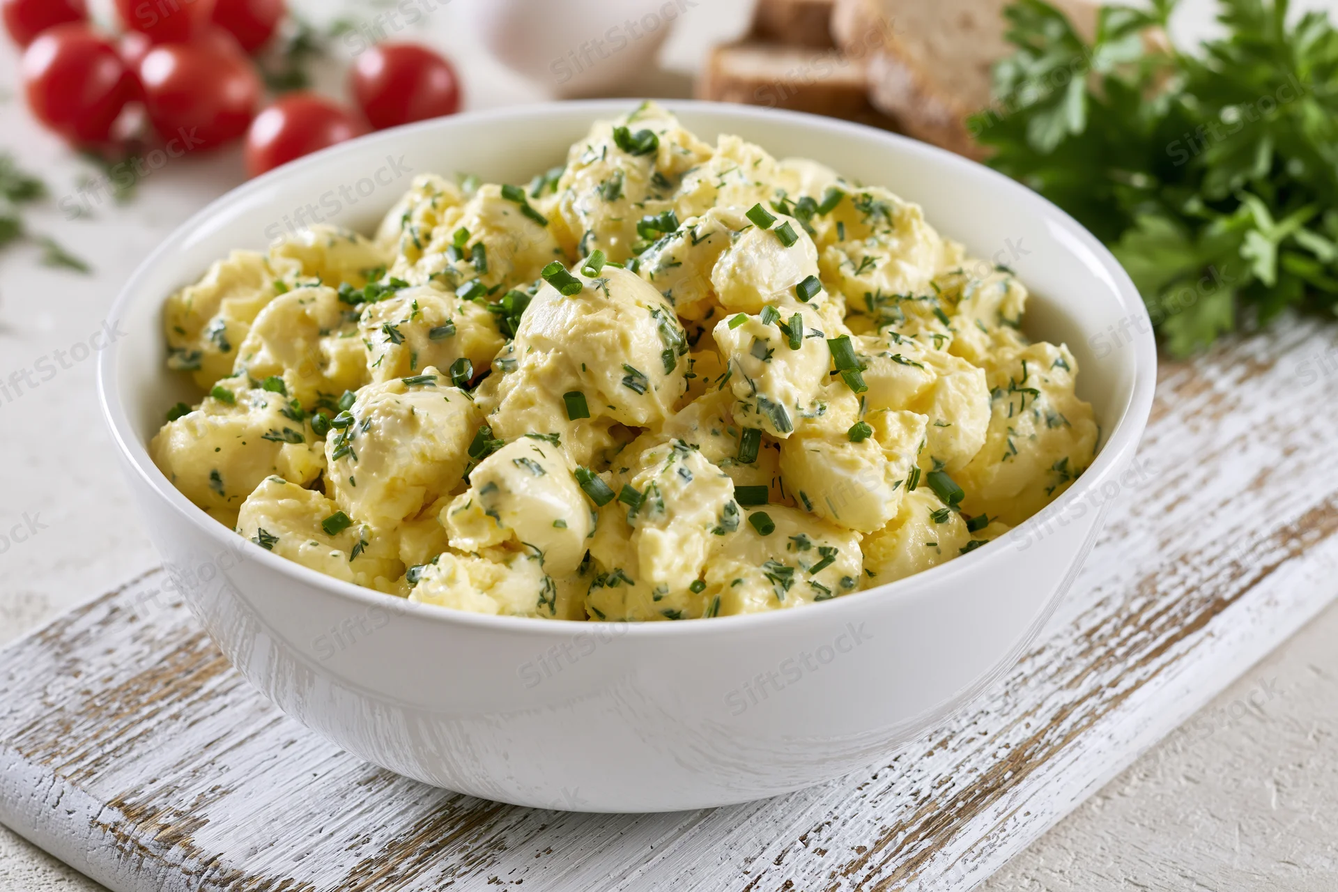 Chunky egg salad with chives in a white ceramic bowl on a rustic wooden board