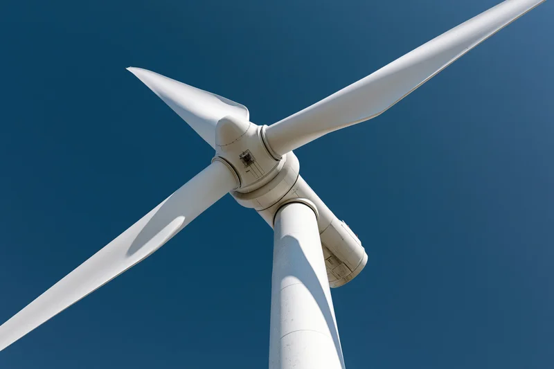 Wind turbine hub with three blades against clear blue sky
