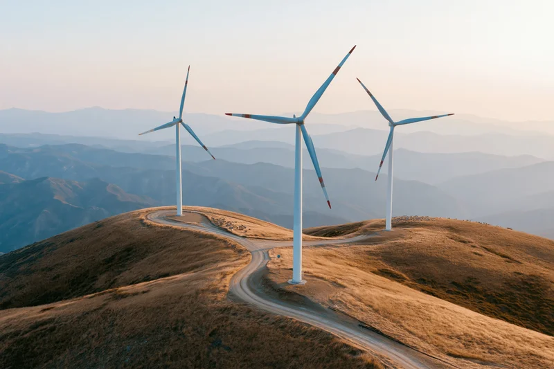 Wind turbines on rolling hilltops with a winding dirt road at sunset
