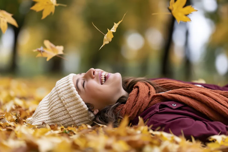 Young woman laughing while lying on her back in a pile of fallen autumn leaves in a park