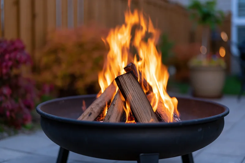 Fire burning in a black metal bowl fire pit on a backyard patio