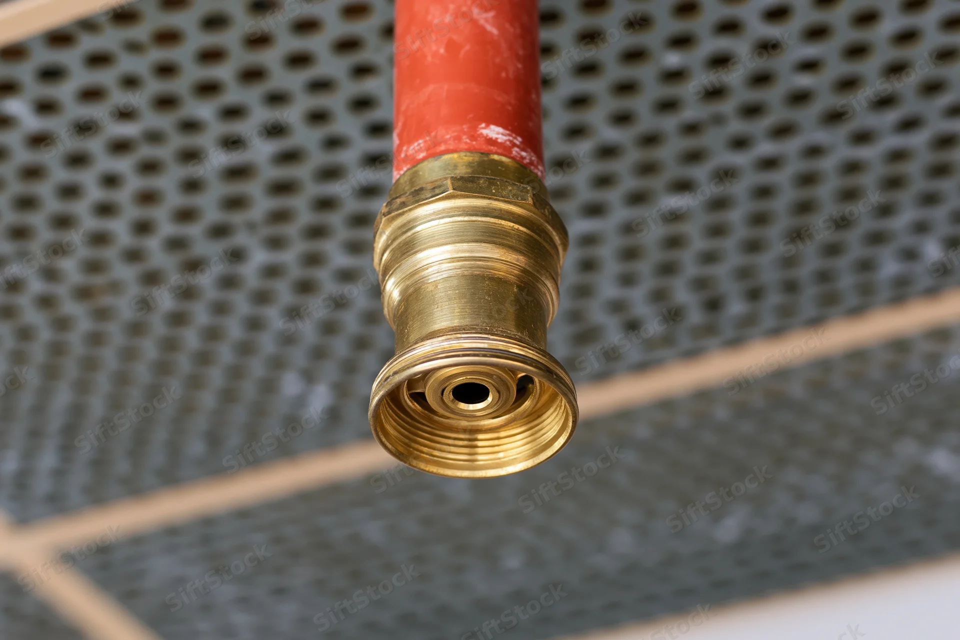 Brass fire sprinkler head mounted on red pipe against perforated ceiling grid