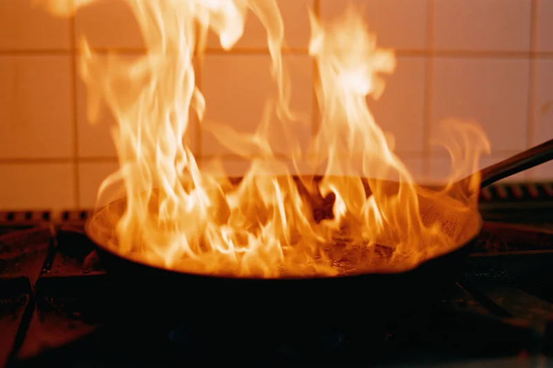 Flames rising from a cast iron pan on a gas stove in a kitchen