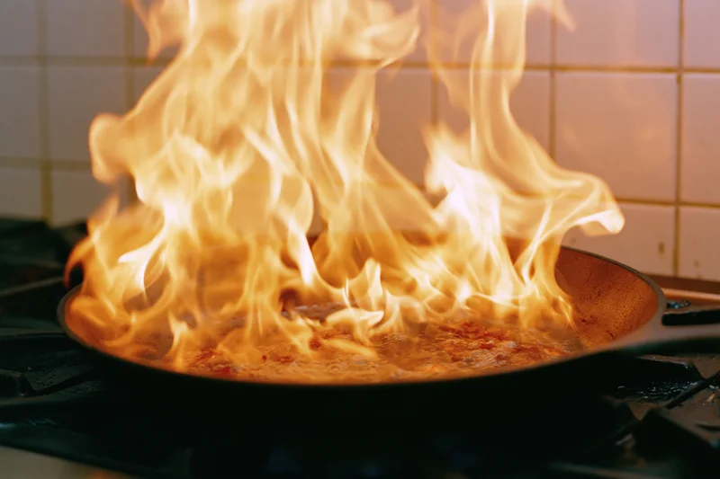 Flames rising from a cast iron pan on a stove during cooking