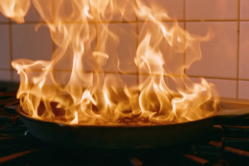 Tall flames rising from a cast iron pan on a gas stove in a commercial kitchen