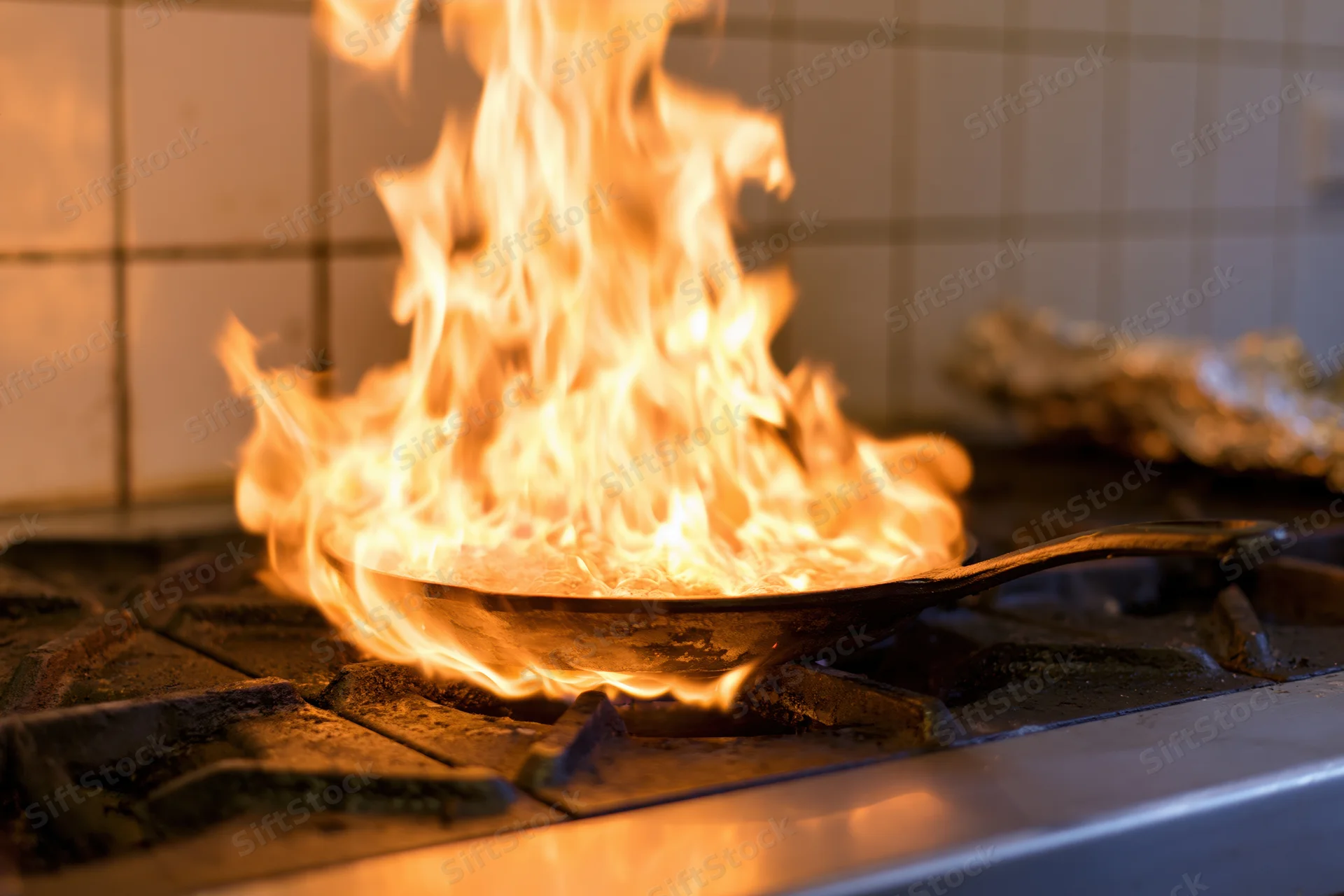 Cast iron skillet erupting in tall flames on a gas stove in a kitchen