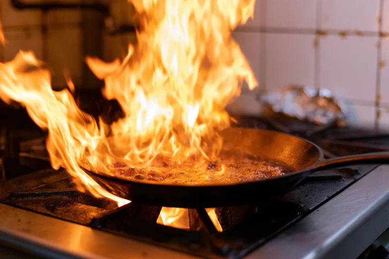 Cast iron skillet with tall flames during cooking on a commercial gas stove