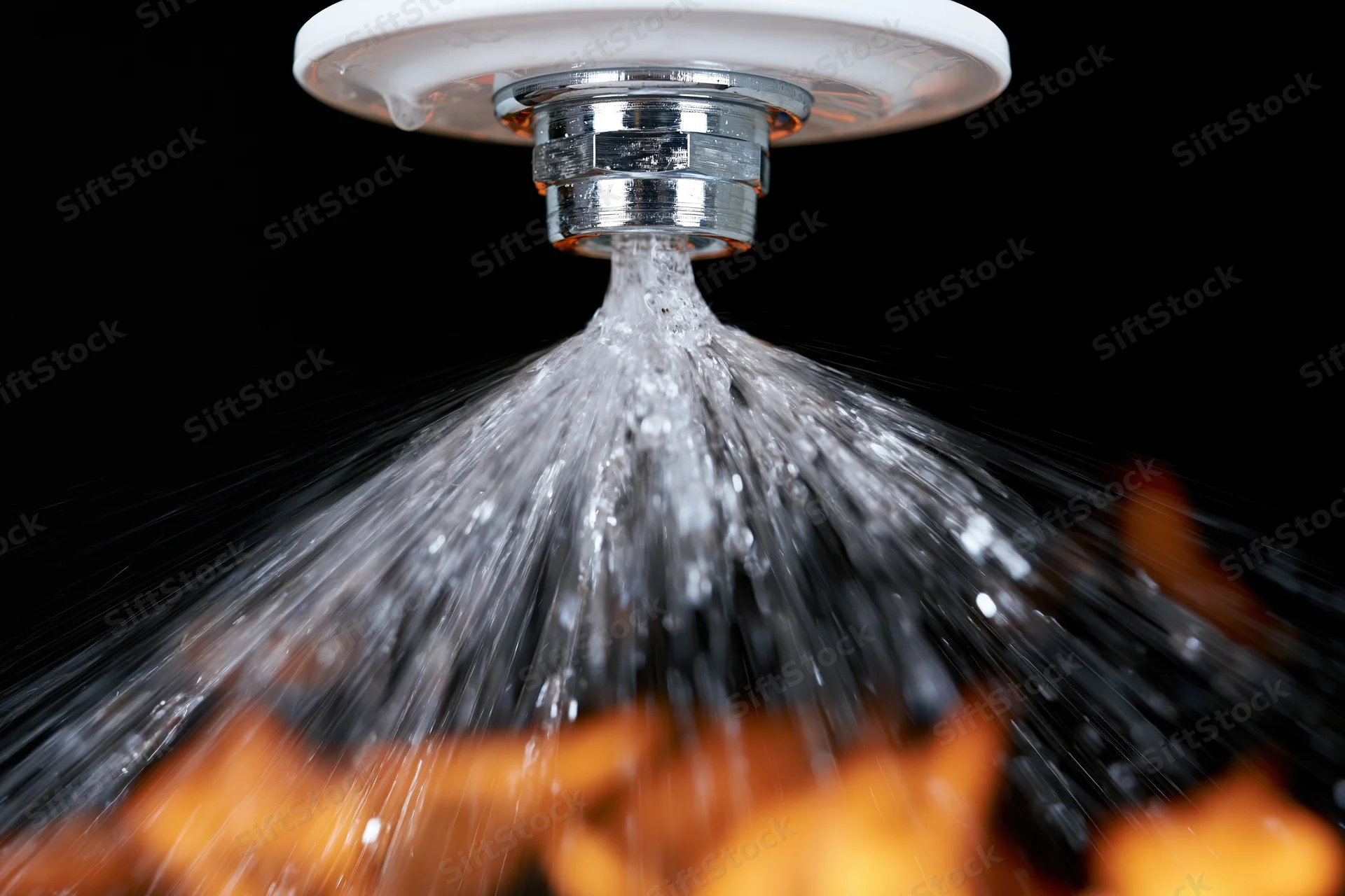 Fire sprinkler head spraying water from a white ceiling plate against black background