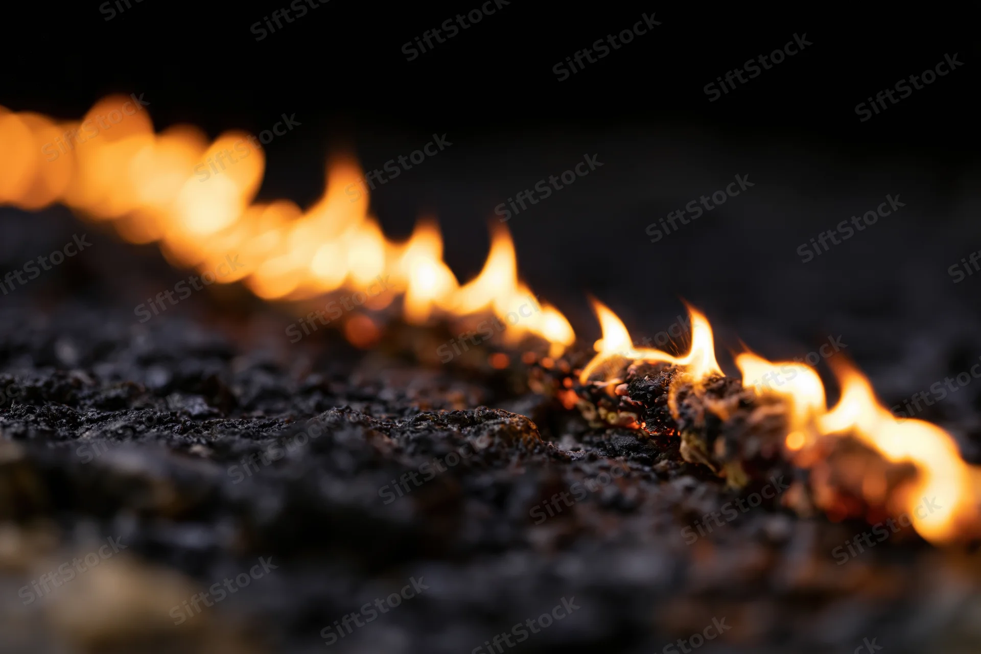Diagonal line of flames burning across a dark textured surface at night