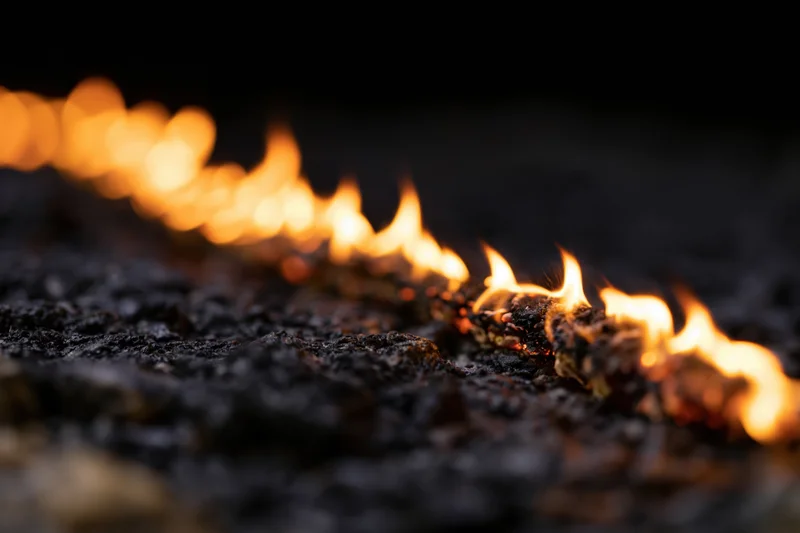 Diagonal line of flames burning across a dark textured surface at night