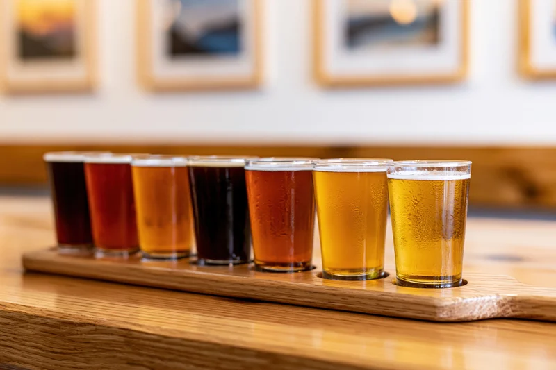 Eight craft beers in small glasses arranged on a wooden tray on a bar countertop
