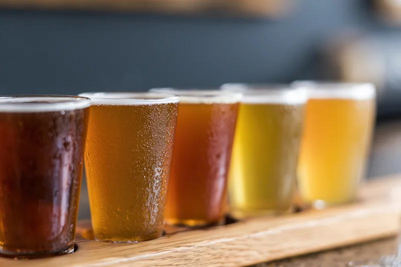 Five craft beers in small glasses arranged in a row on a wooden tray for tasting