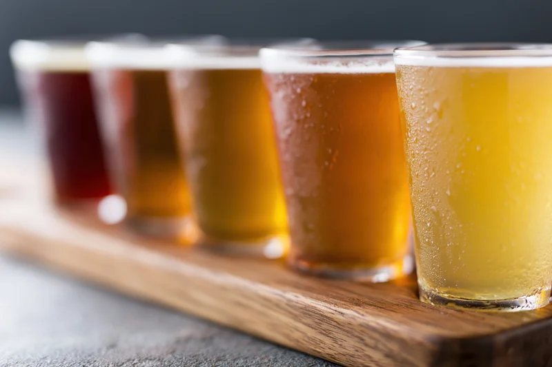 Five craft beers in small glasses arranged in a row on a wooden tray