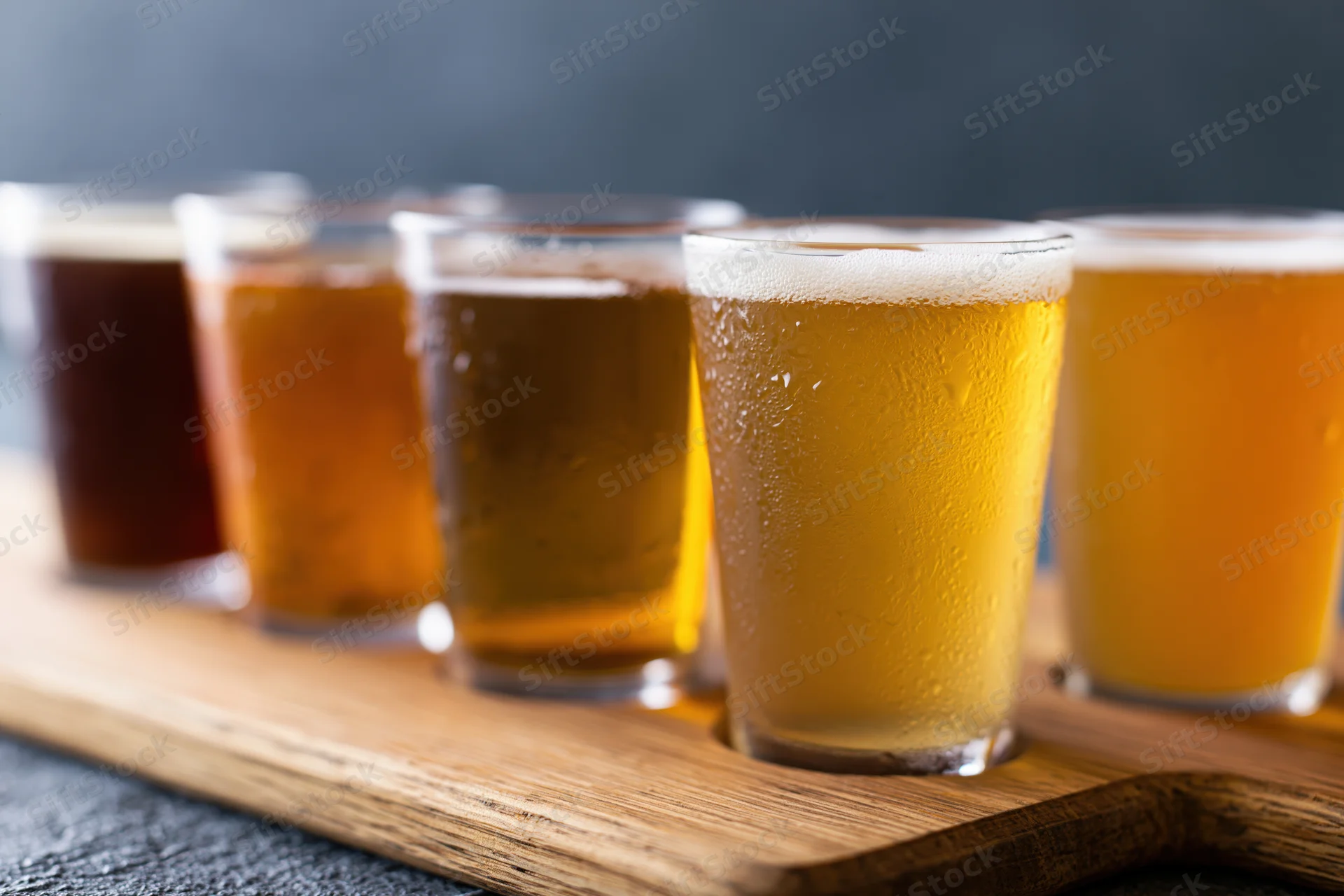 Five craft beers in small glasses arranged in a row on a wooden tray